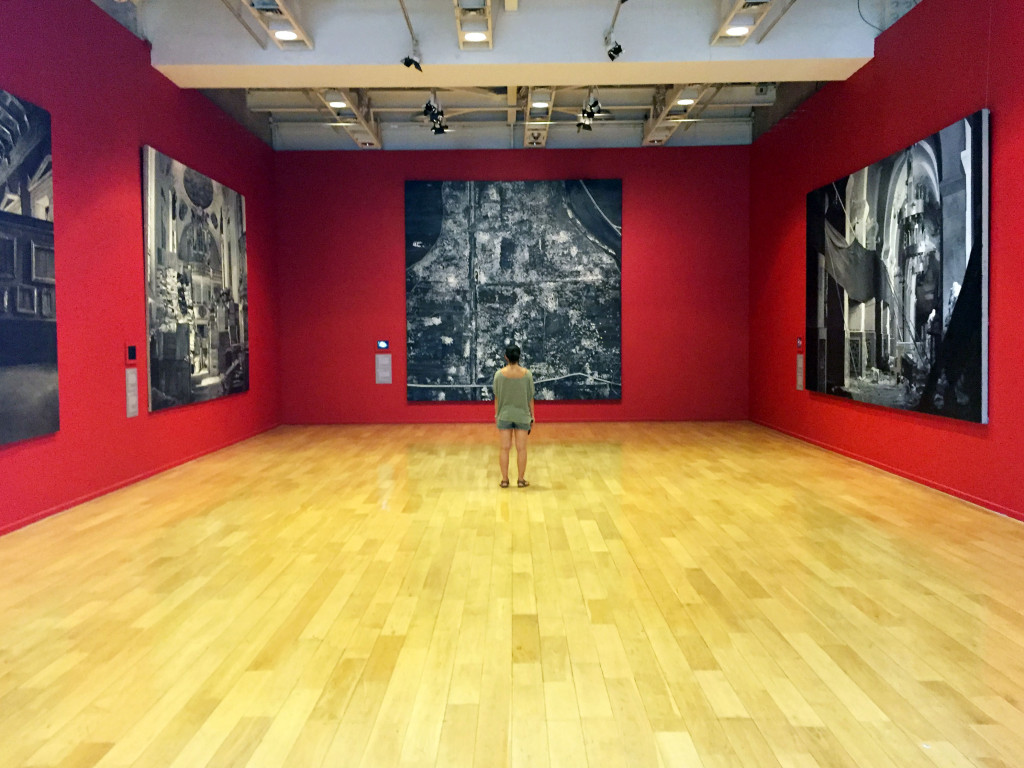 Far wall, painting showing all the illegal excavation of artifacts in Syria, accompanied by a stop motion film on the screen to the painting's left.